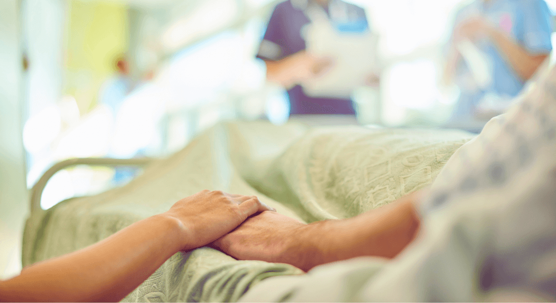 Photograph of two people holding hands in a hospital bed