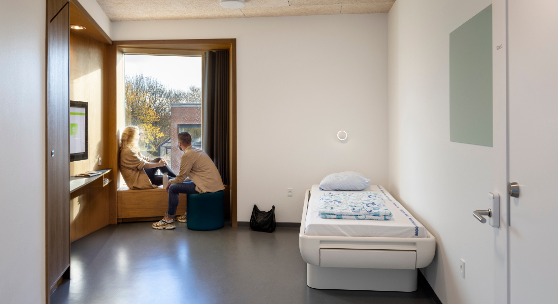 Two people sitting by a window in a bed section of a psychiatric ward