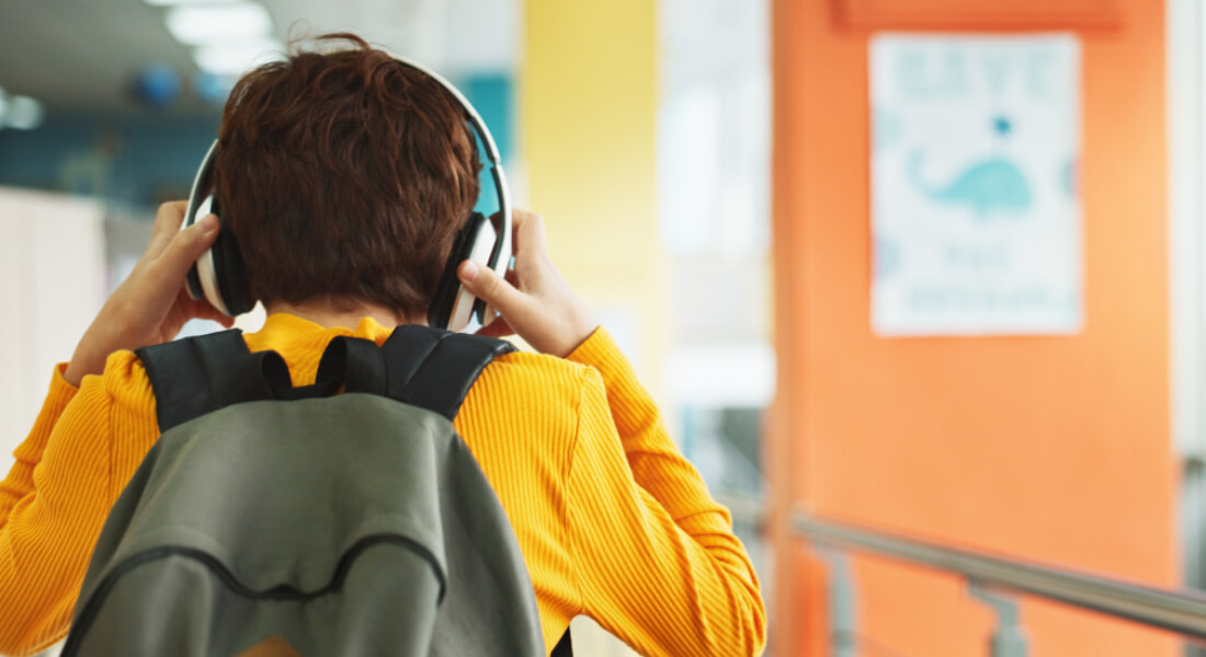 A child seen from behind with headphones on holding his head.
