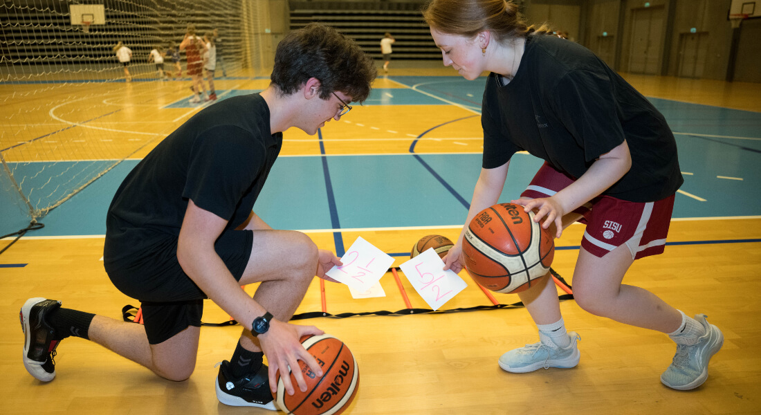 To children dribbling a basketball each while picking up notes with fractions written on them