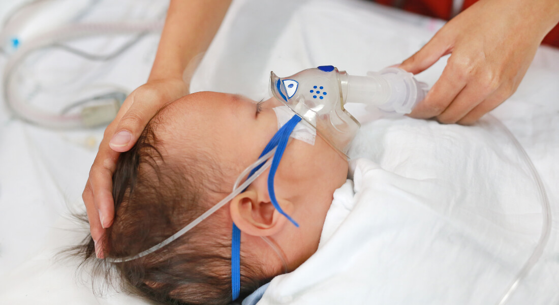 An infant in a hospital bed with a respiratory aid on.