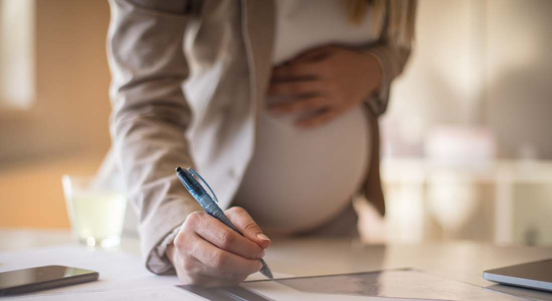 A pregnant woman bending forward to sign some papers